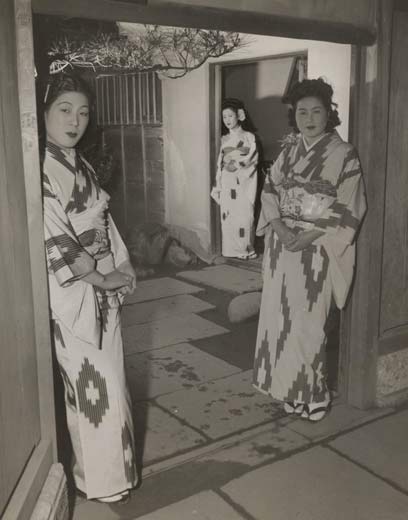 Photographic image of three well-dressed Jaapnese women waiting at the entrance to an upstairs brothel in Tokyo.