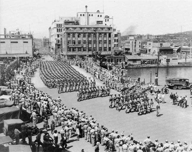 Photograph of US troops parading through a Japanese street.