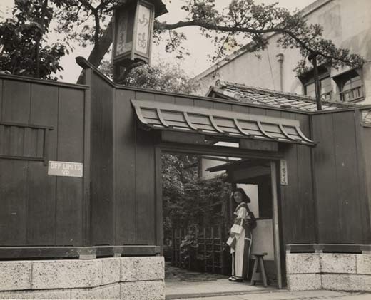 Photographic image of an established house of prostitution.  In the doorway is a Japanese woman dressed in traditional clothing and on the wall is a sign written in English that reads 'Off Limits VD'